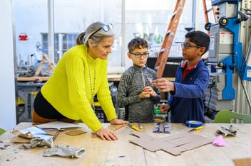excited fourth grade teacher sitting next to a boy’s desk in a classroom