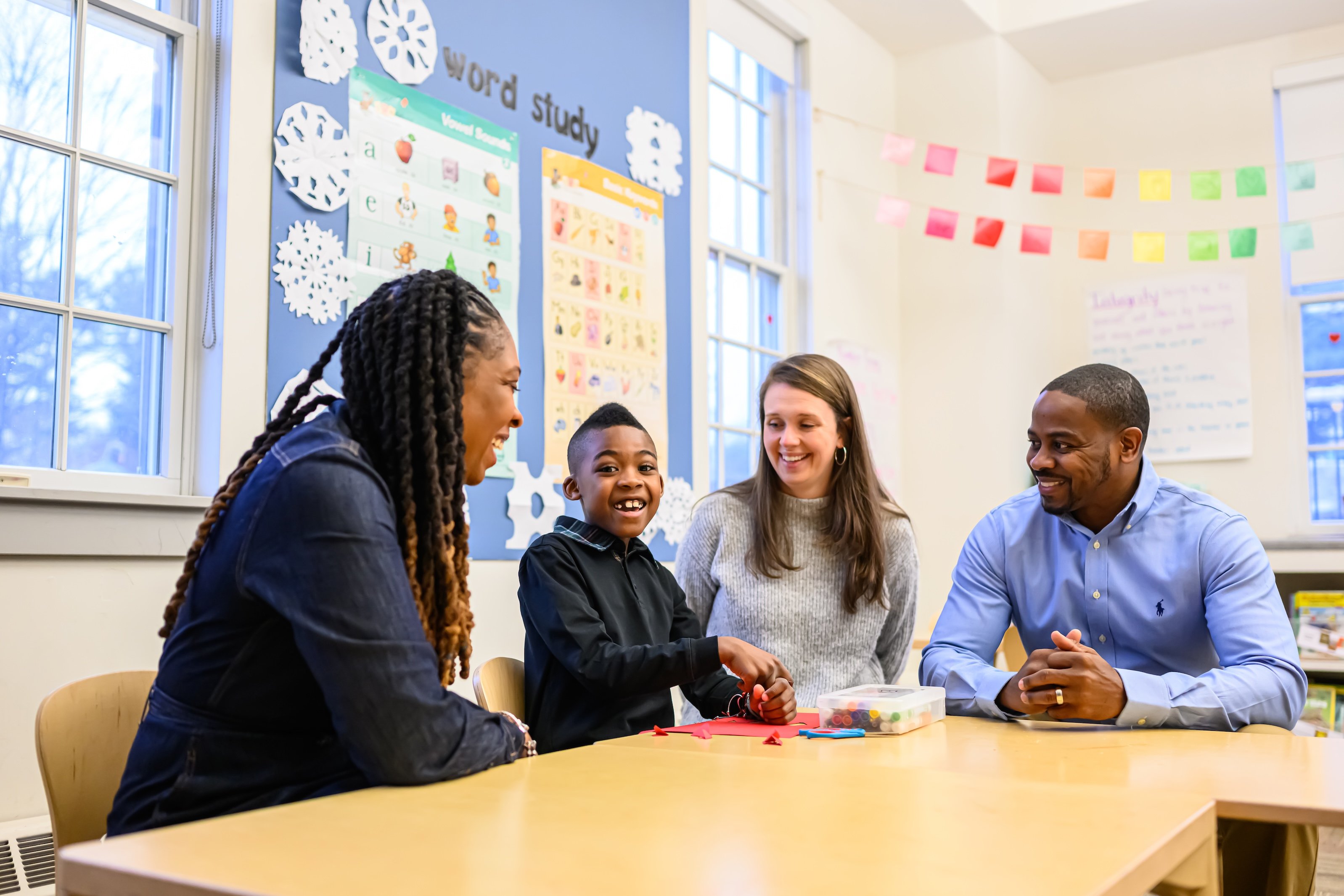 A teacher sitting down and laughing with a child and his two parents.